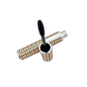 Textured Gold Mascara Tube – a cylindrical gold-tone case has a repeating raised-looking grid texture across both body and cap